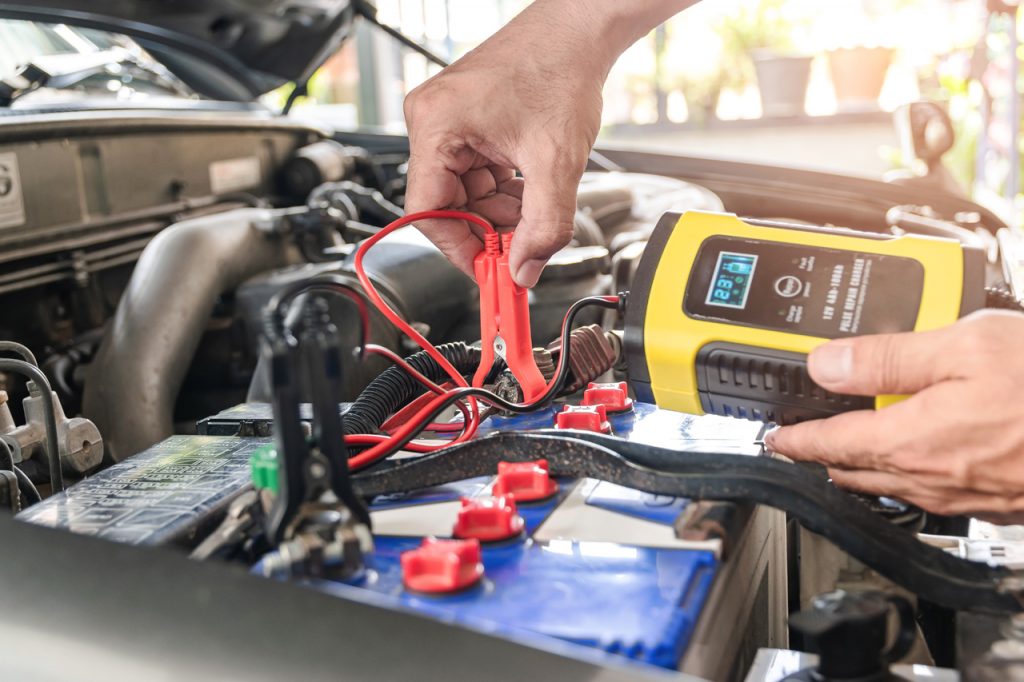 Tow Truck Operator With Voltmeter Performing Car Jump Start Service