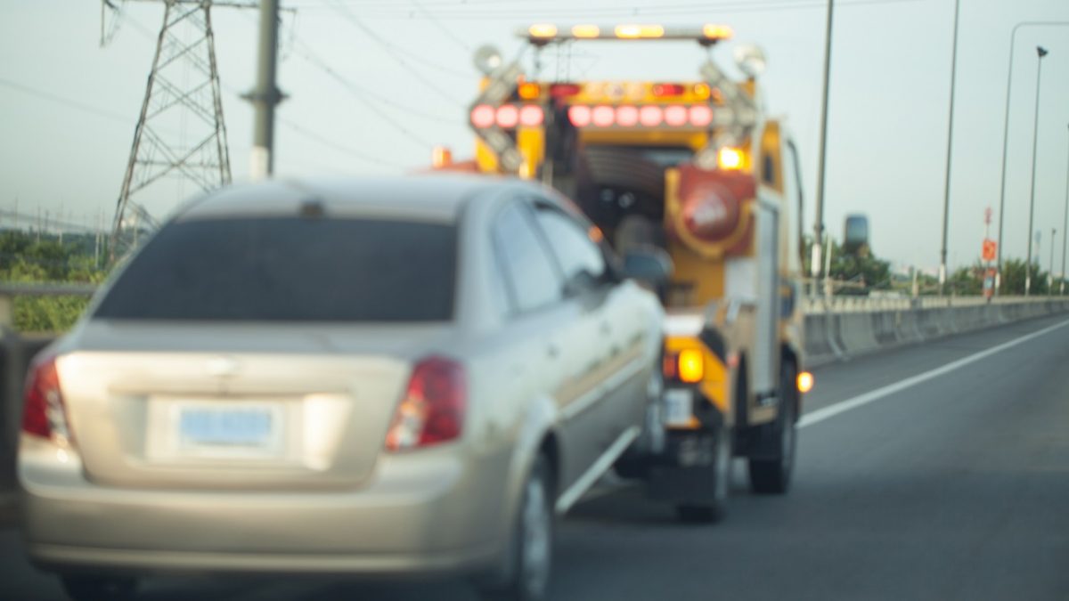 Wheel lift tow truck towing a small sedan on the highway